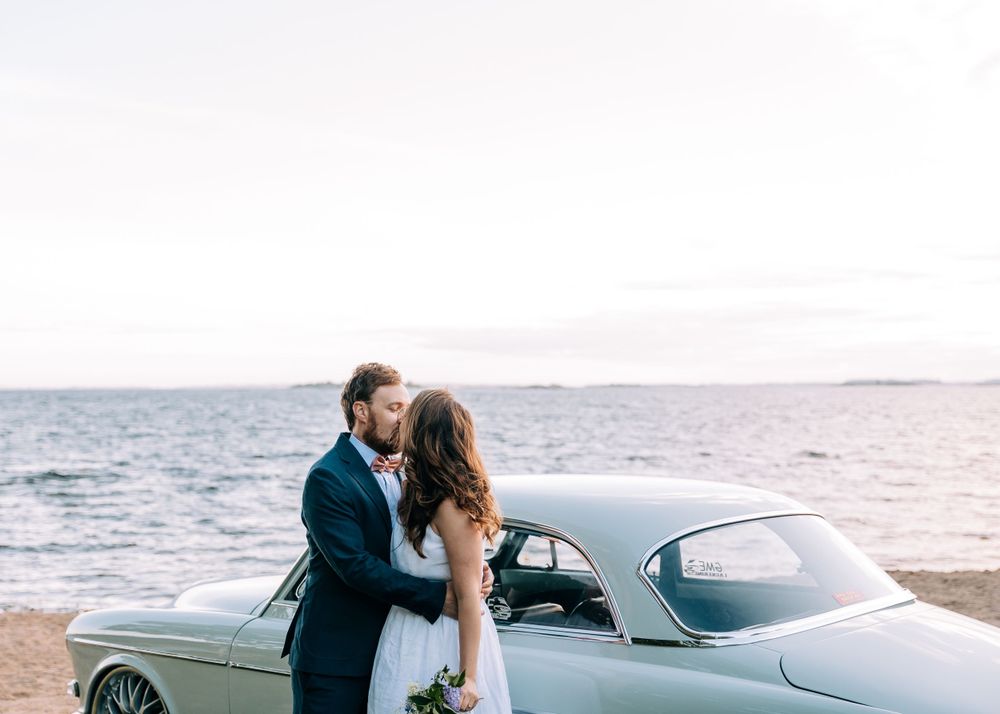 Classic vintage car parked by the ocean during a romantic wedding photoshoot at sunset.