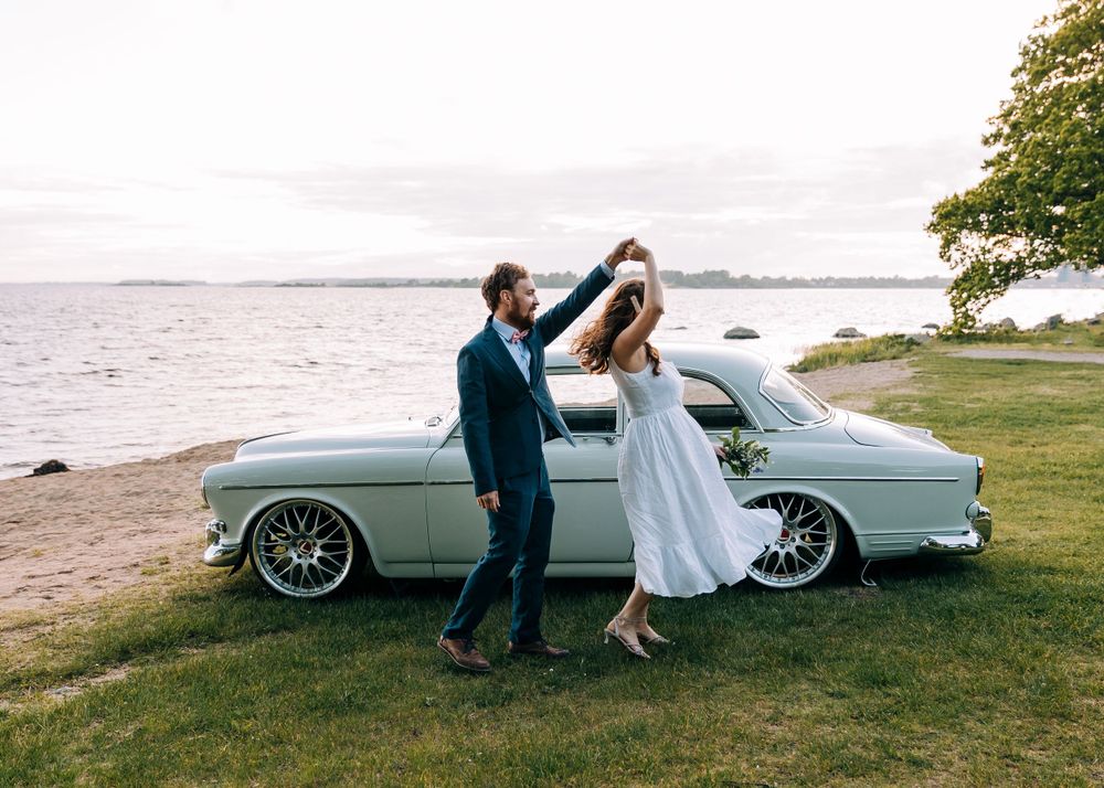Elegant couple dancing next to vintage car by seaside.
