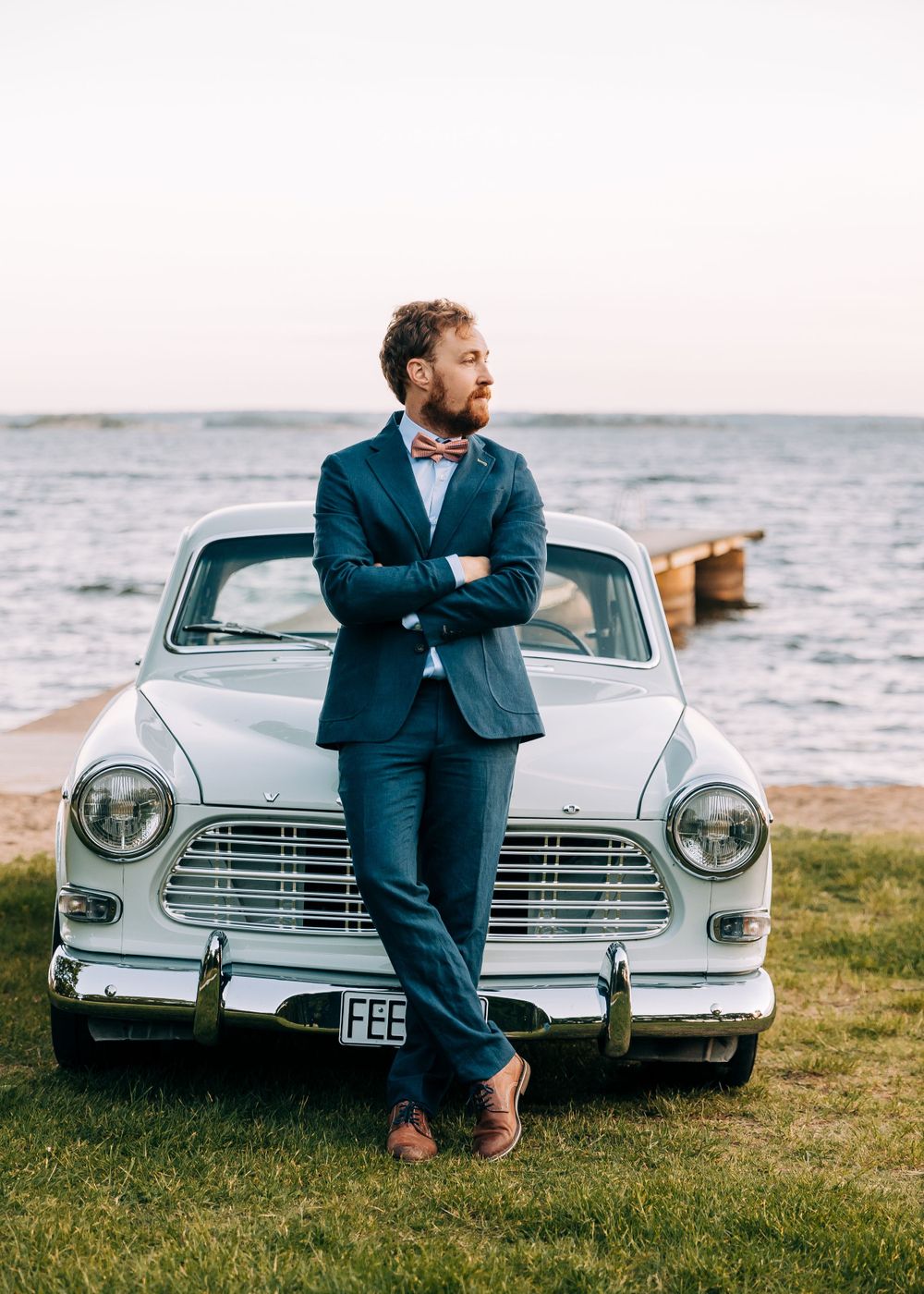 Classic white Volvo car parked by the seaside with navy-suited figure.