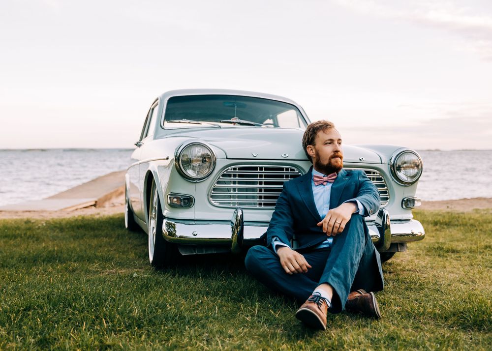 Vintage white Volvo car parked on coastal grass during sunset.