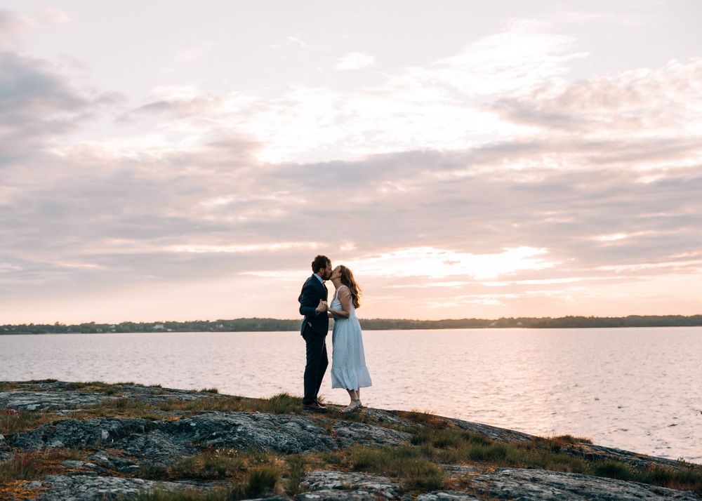 Silhouetted couple standing on rocky shore during sunset.