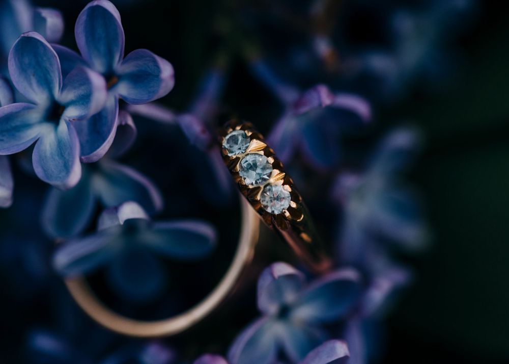 Engagement ring with diamonds photographed against purple lilac flowers.