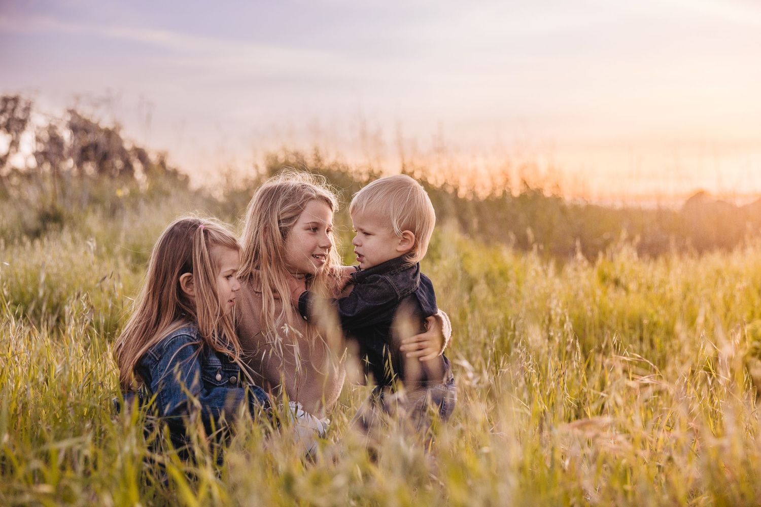 Three people sharing a tender moment in a sunlit wildflower field.