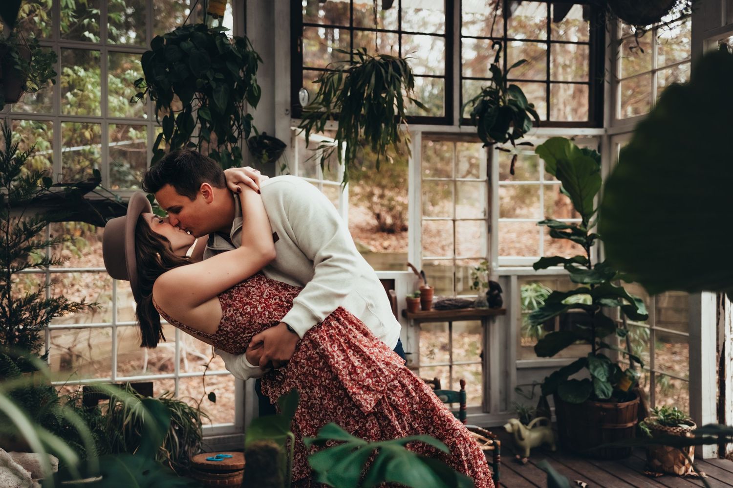 man dips wife in a greenhouse and kisses her during couples photo session