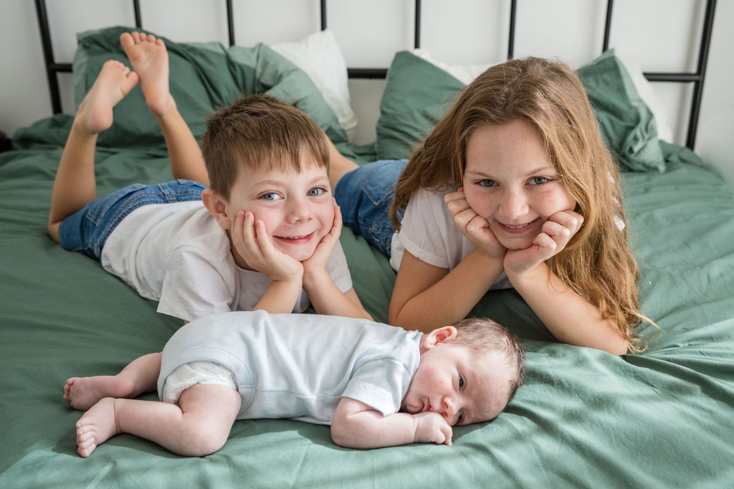 siblings with newborn brother on bed