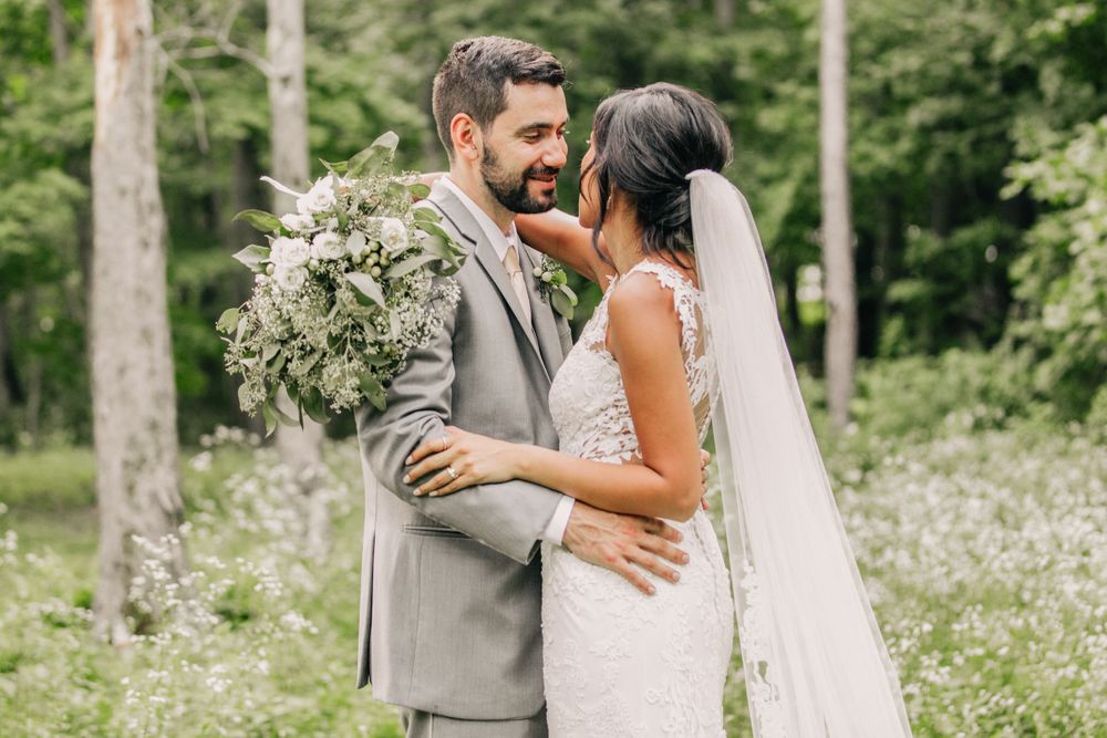 A tender moment between newlyweds in a forest setting with a lush white floral bouquet.