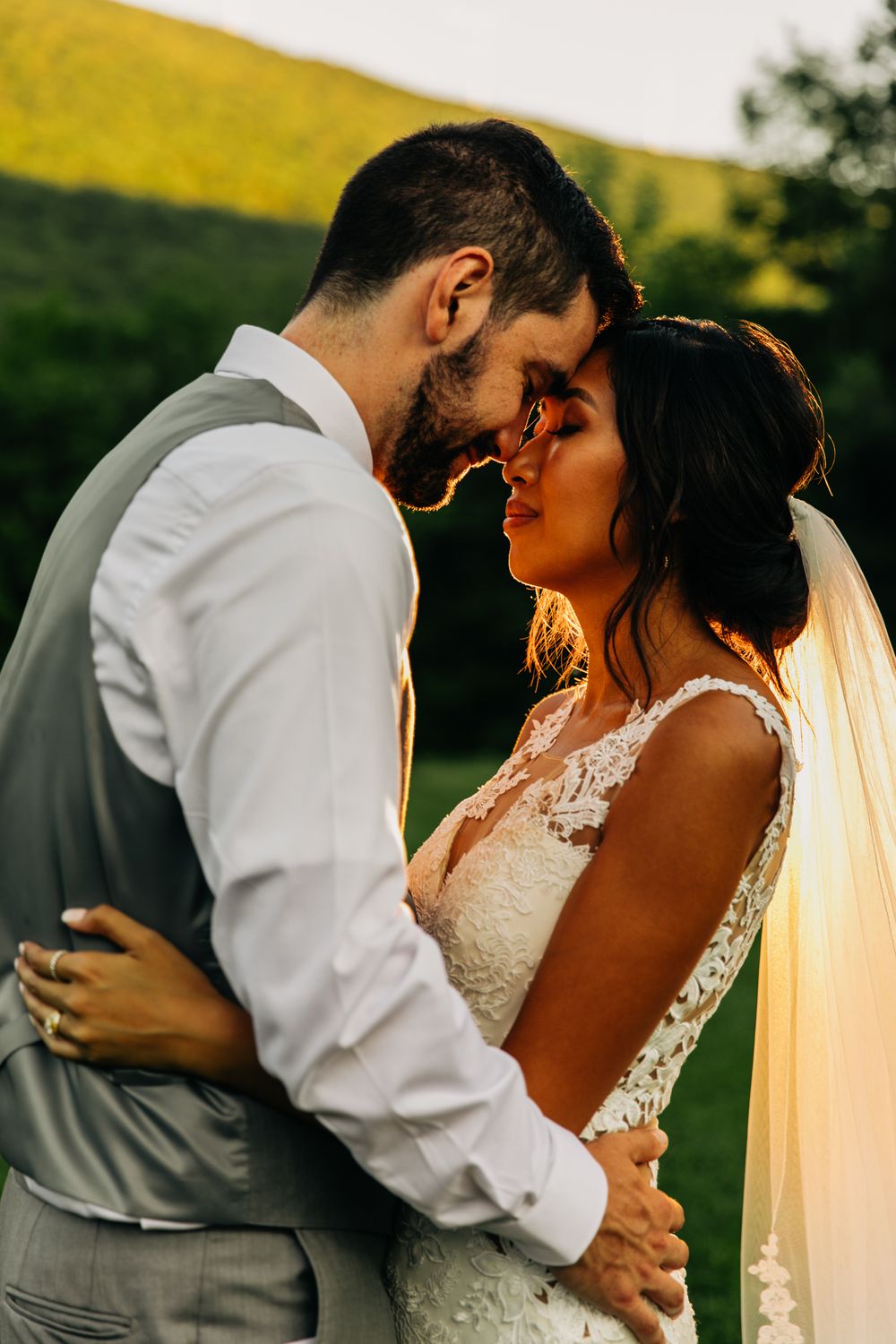 Intimate sunset portrait of newlyweds embracing in golden light with flowing veil.