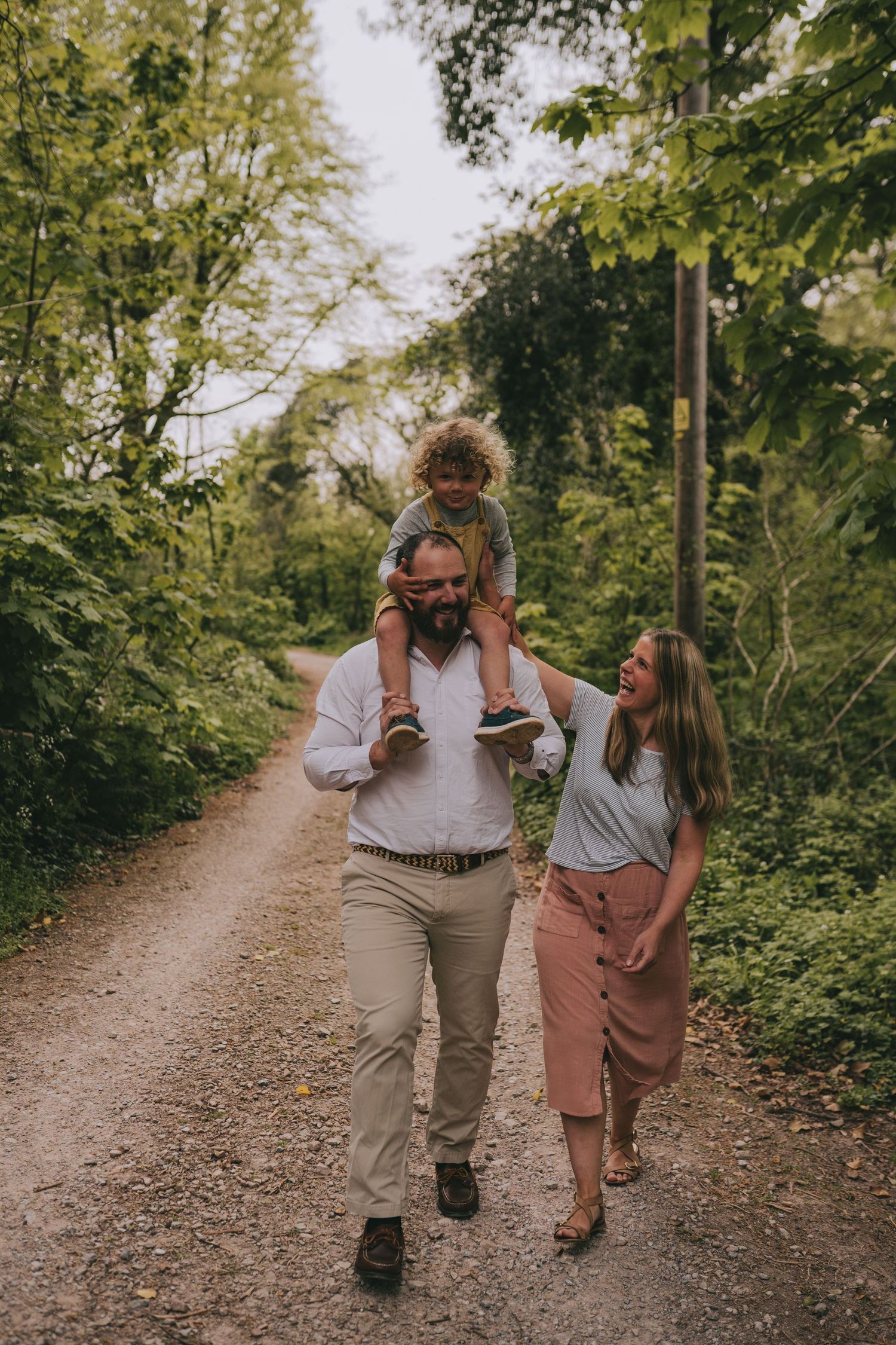 A family walking together on a tree-lined dirt path on a sunny day.