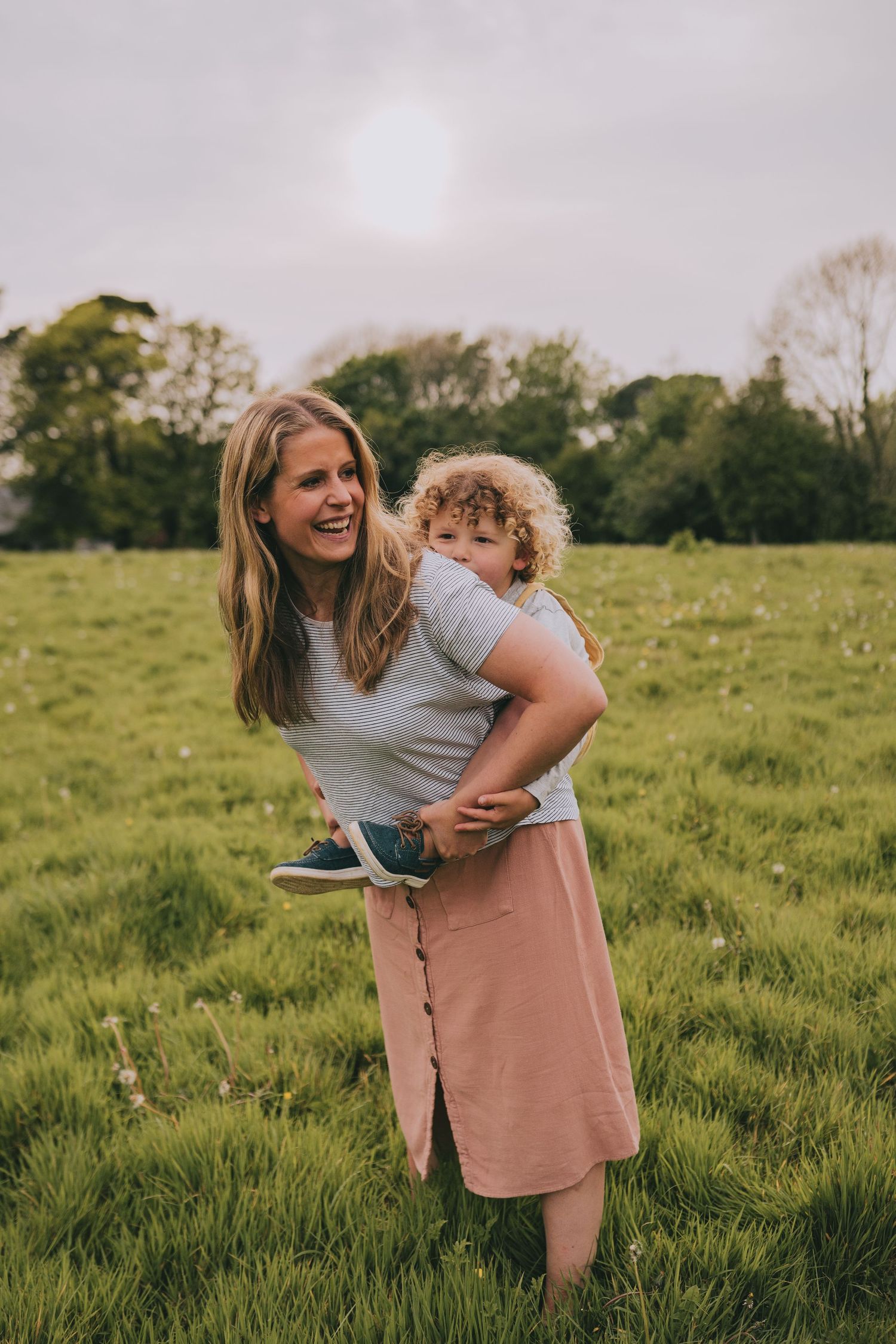 Parent and child share joyful moment together in sun-drenched meadow with green grass.