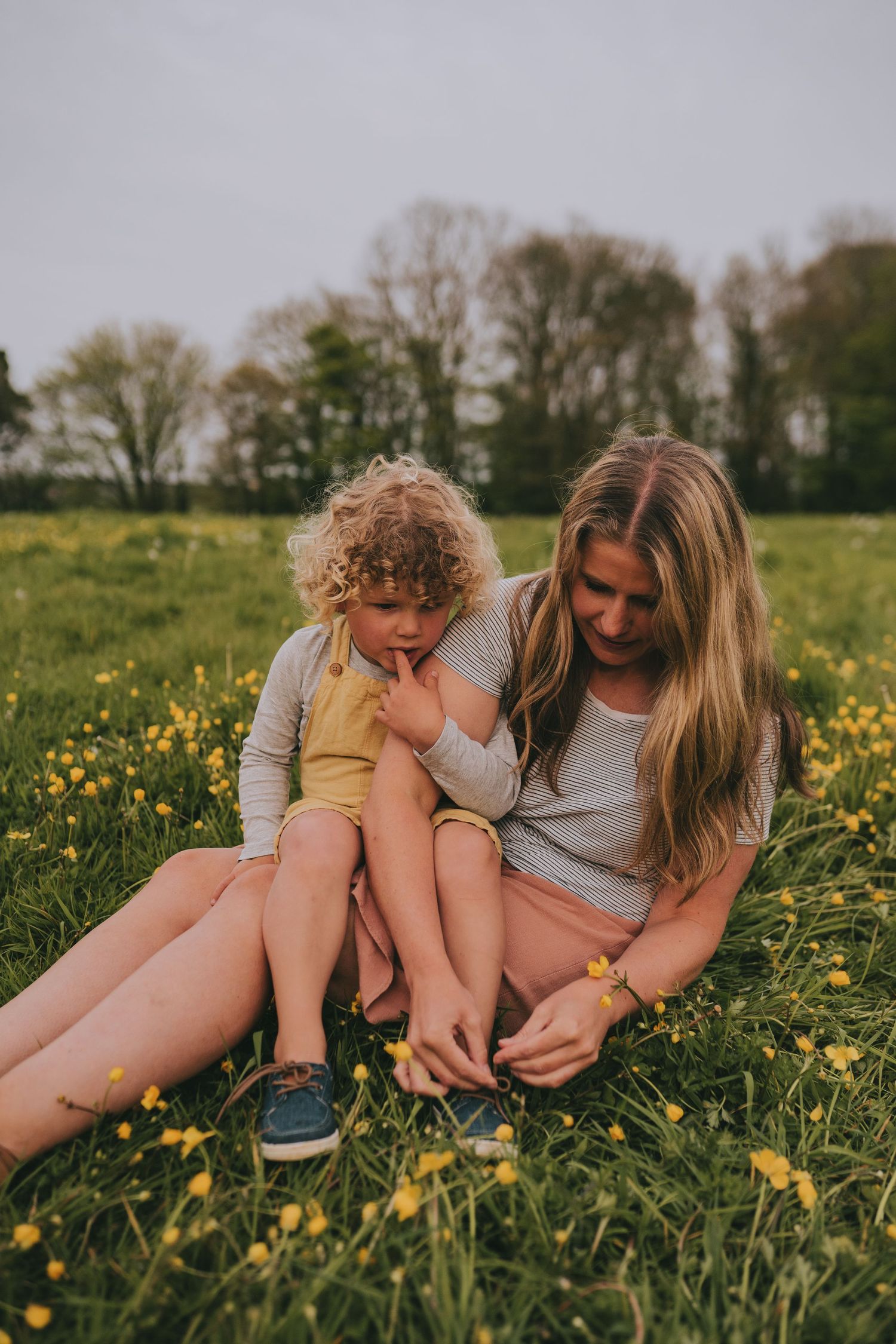Parent and child sitting together in field of yellow wildflowers during golden hour.