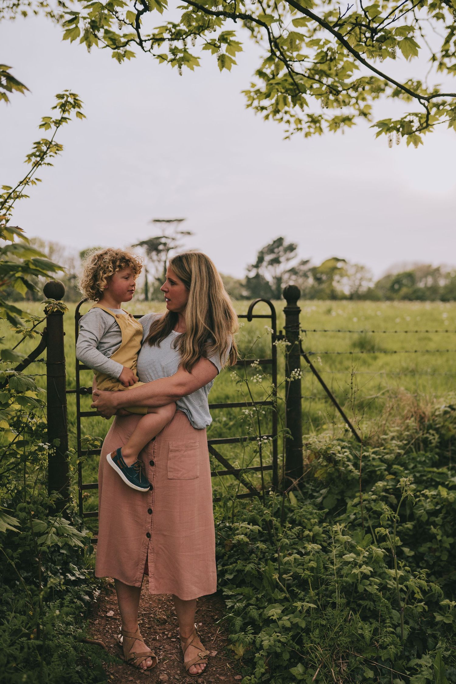 Tender outdoor moment between parent and child by rustic fence in countryside setting.