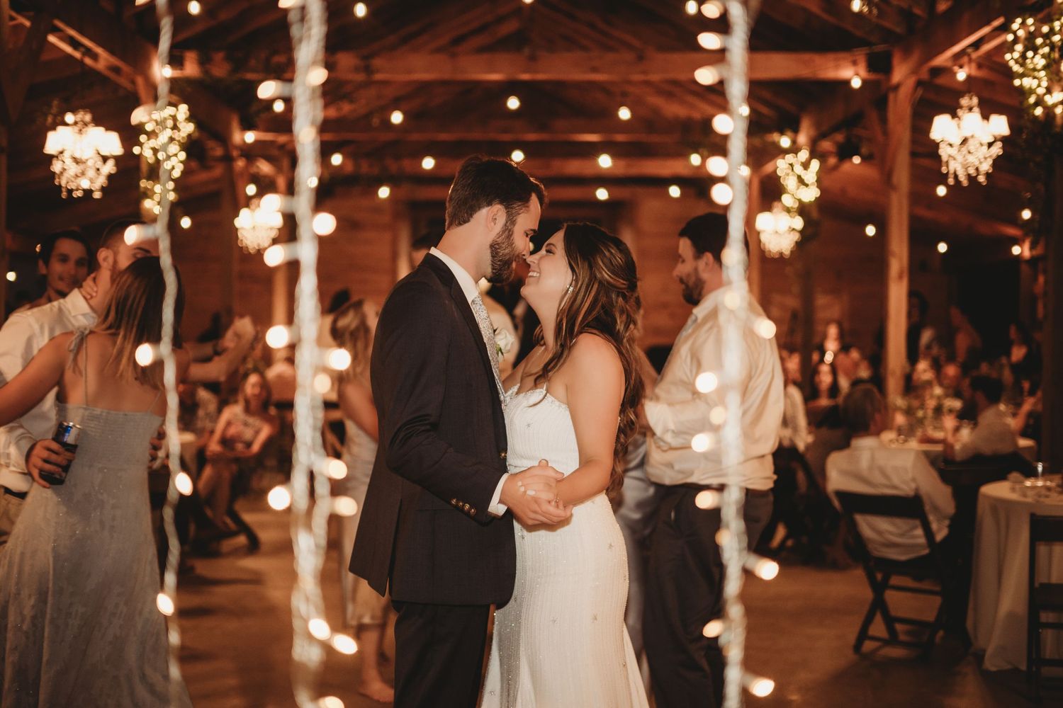 Rustic barn wedding reception venue decorated with twinkling string lights and chandeliers.