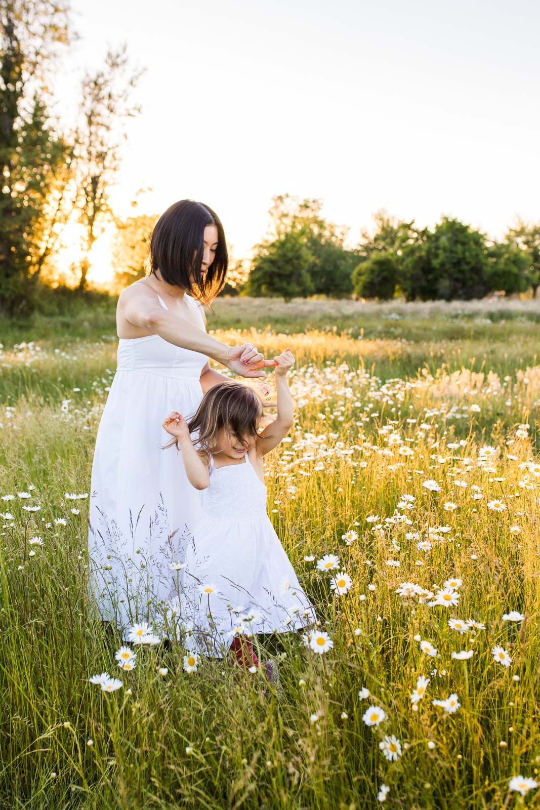 Mother twirling daughter in a daisy field at sunset
