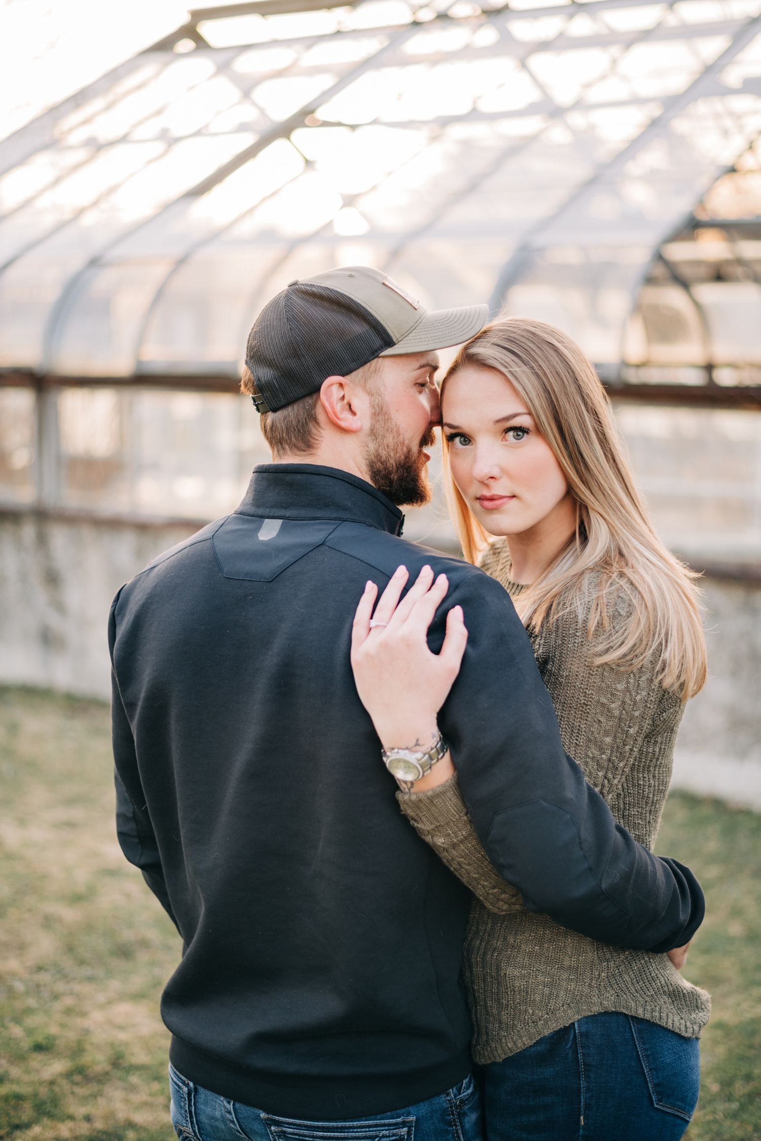engaged couple hugging, woman looking over man's shoulder at camera