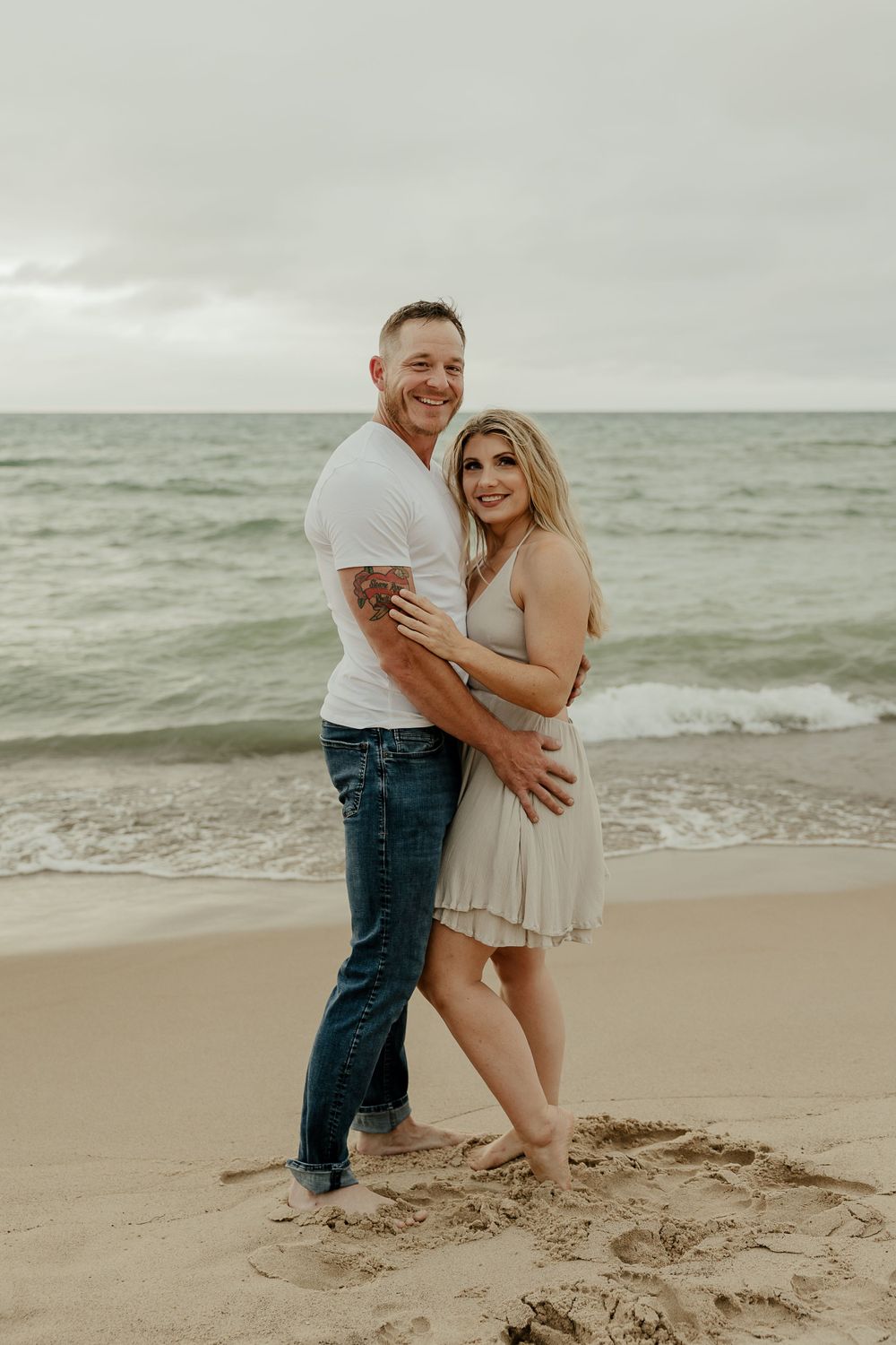 Candid beach photo of couple in casual wear standing together on sand.