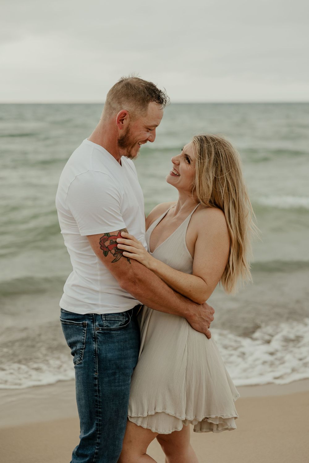 Romantic beach portrait of couple embracing on cloudy day by ocean.