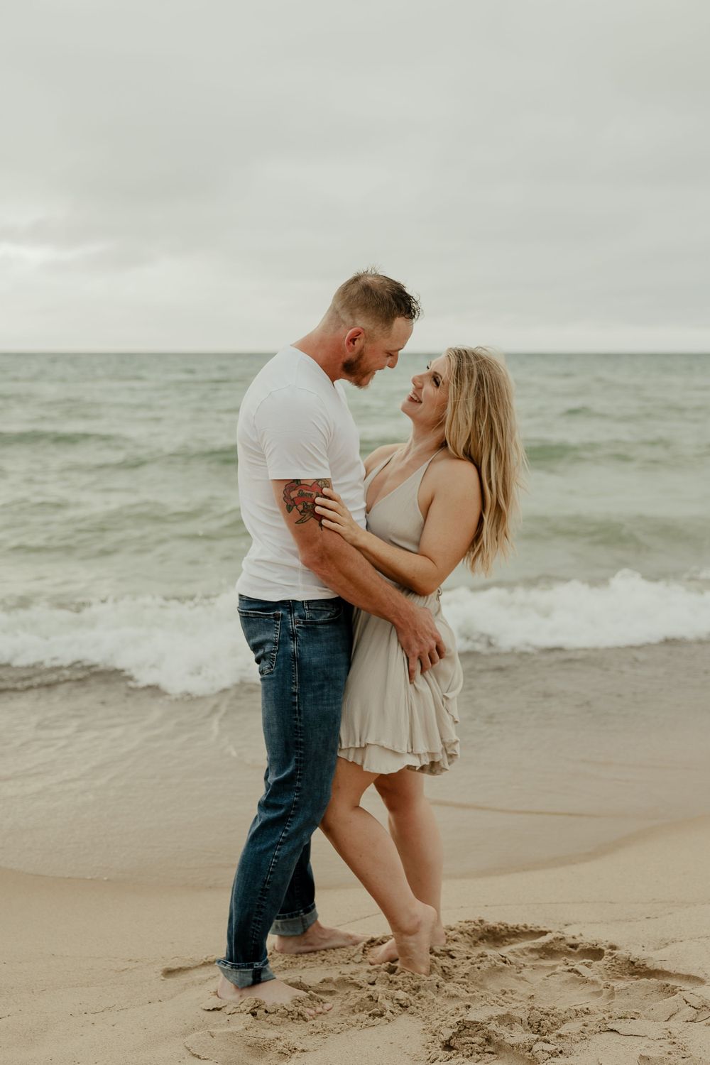 Intimate couple portrait on beach with waves and overcast sky in background.