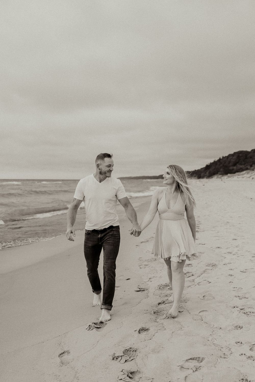 A black and white photo captures a couple walking together on a peaceful beach.