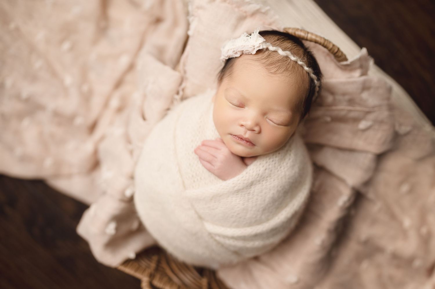 Professional newborn portrait with baby wrapped in cream colored fabric on textured background.
