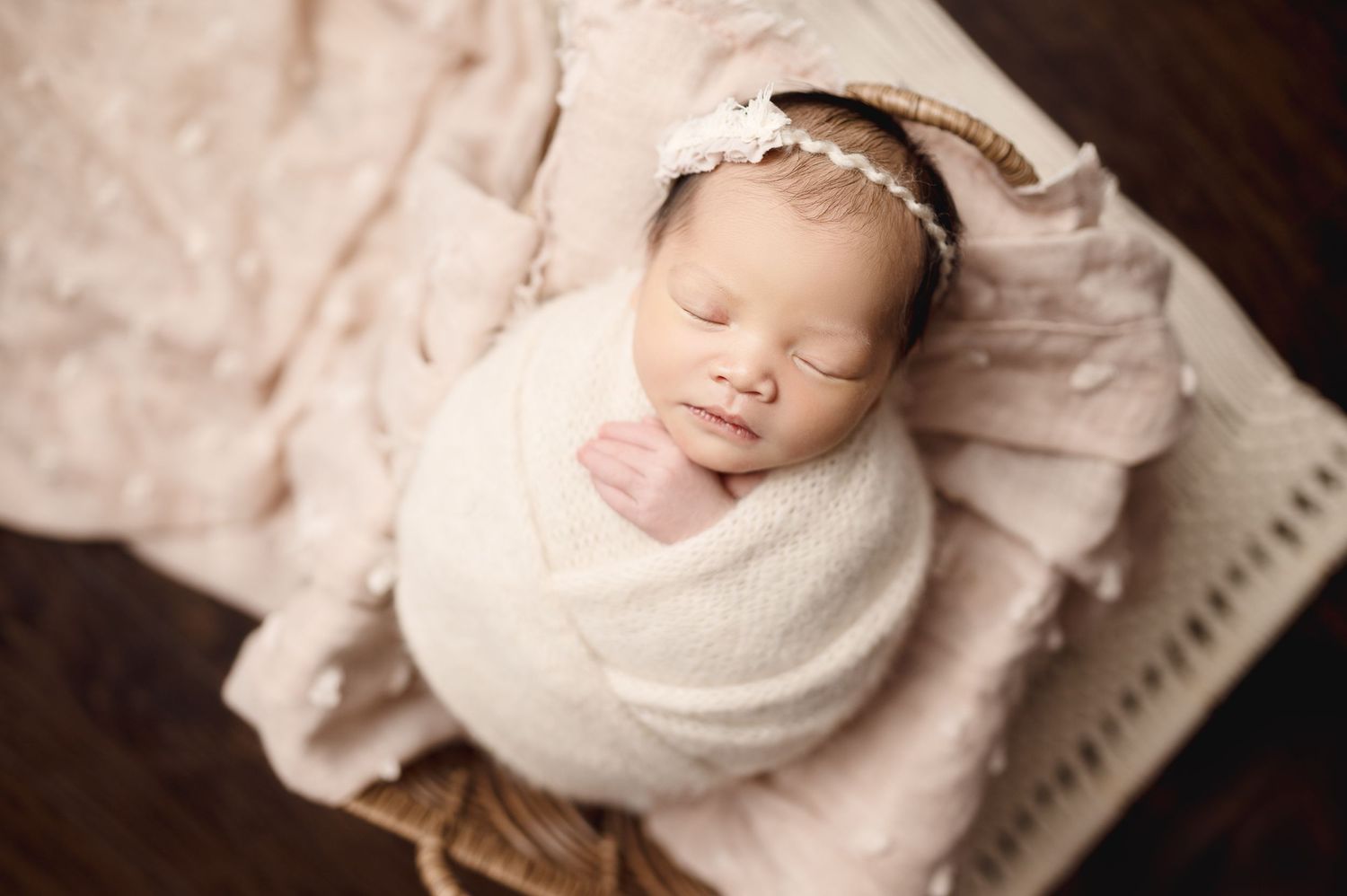 Peaceful sleeping newborn wrapped in cream fabric with lace headband.
