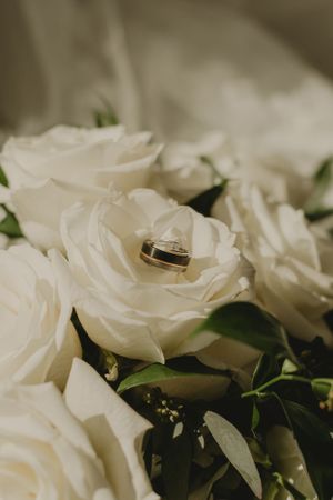 Wedding ring nestled in white rose petals with soft natural lighting.