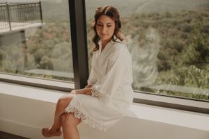 Person in white robe sits thoughtfully on windowsill overlooking mountain landscape.
