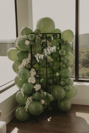 Elegant green balloon and floral installation display against window with 'Mr & Mrs' signage.
