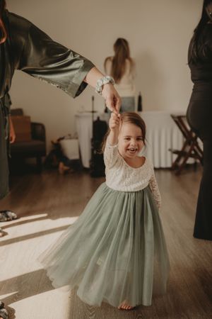 Young child in a flowing mint green dress twirling and dancing in a sunlit room.