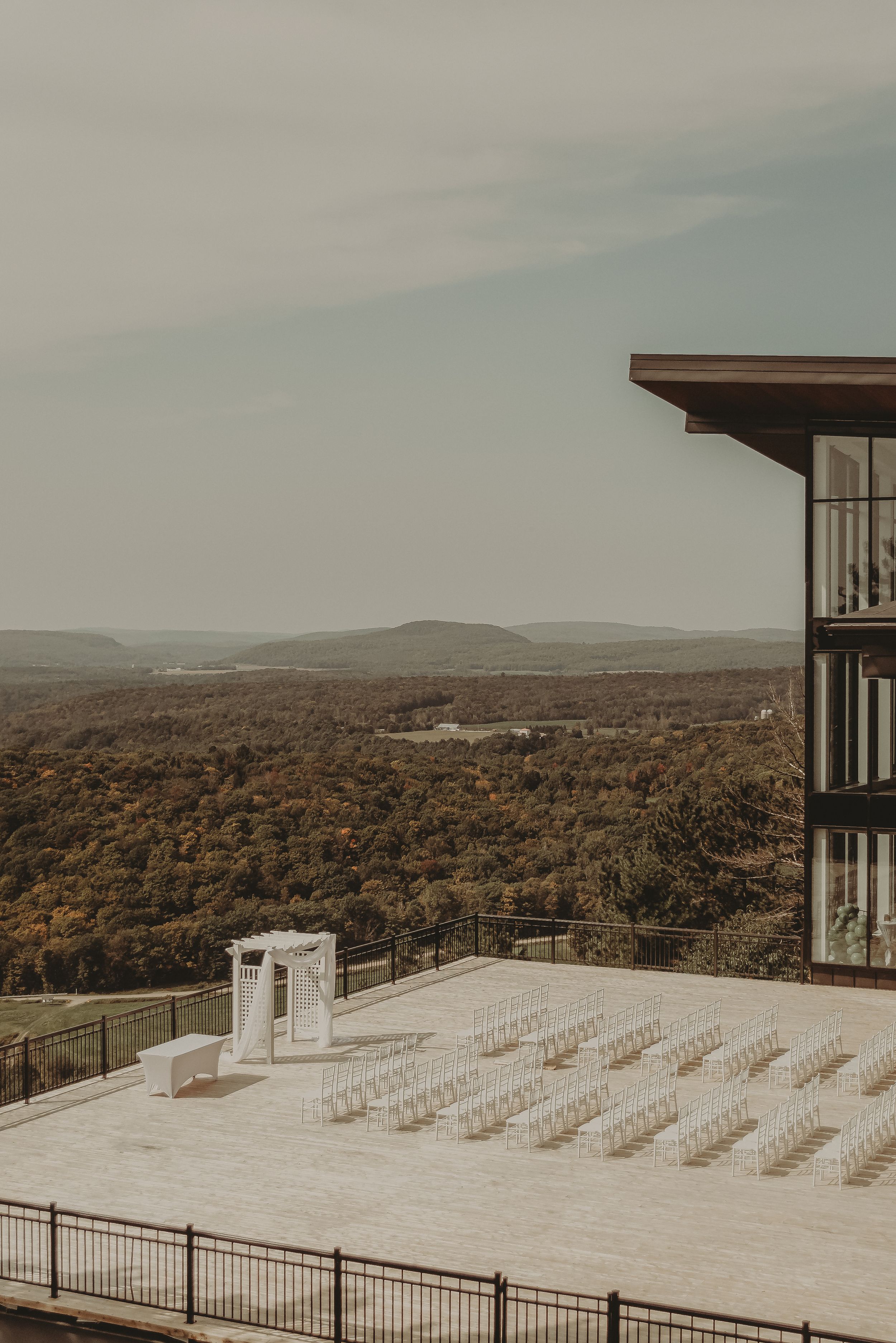 Outdoor wedding venue with white chairs overlooking a scenic mountain landscape at sunset.