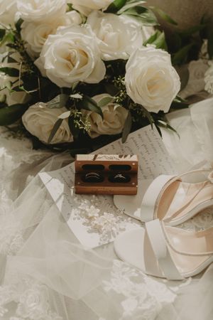 White roses and wedding accessories artfully arranged with wooden ring box.