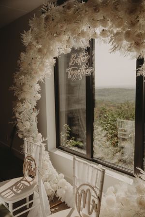 White floral arch with neon sign decorates window space at wedding venue.