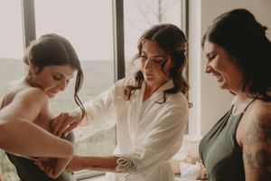 Wedding preparation scene with people helping with final touches in white and sage robes.