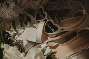 Wedding shoes with heart details arranged among white flowers and greenery.