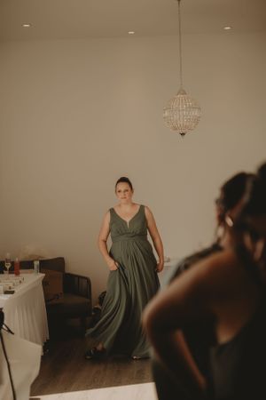 Wedding preparation scene showing someone in an elegant sage green dress under a crystal chandelier.