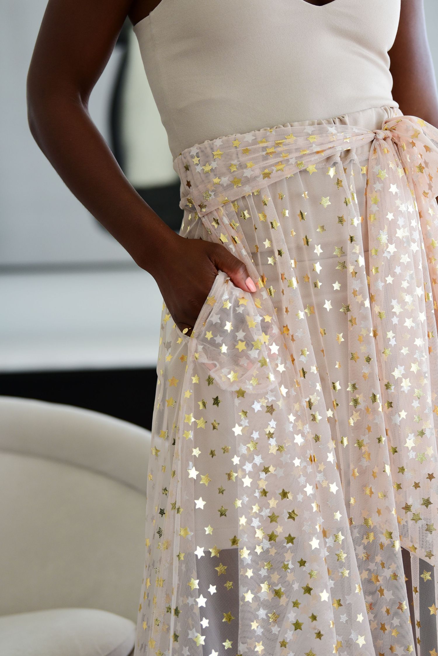 Close-up of a shimmering tulle skirt with metallic star pattern and side pockets in soft peach tones.