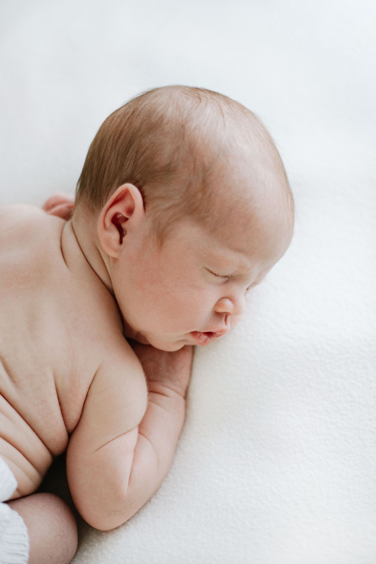 Peaceful sleeping newborn lying on white background in natural light.