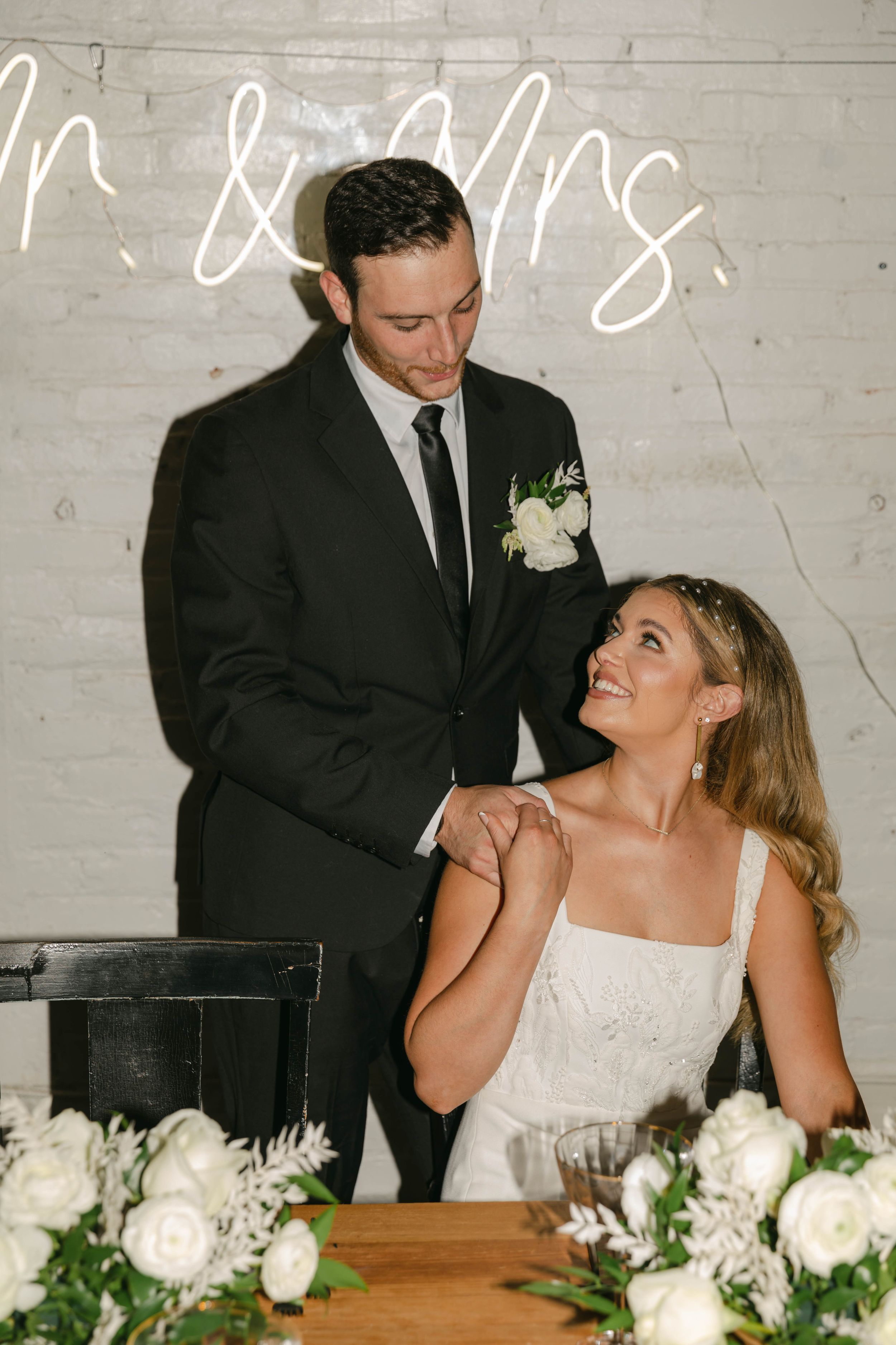 Bride and groom share candid laughing moments at their wedding reception with white floral centerpieces.
