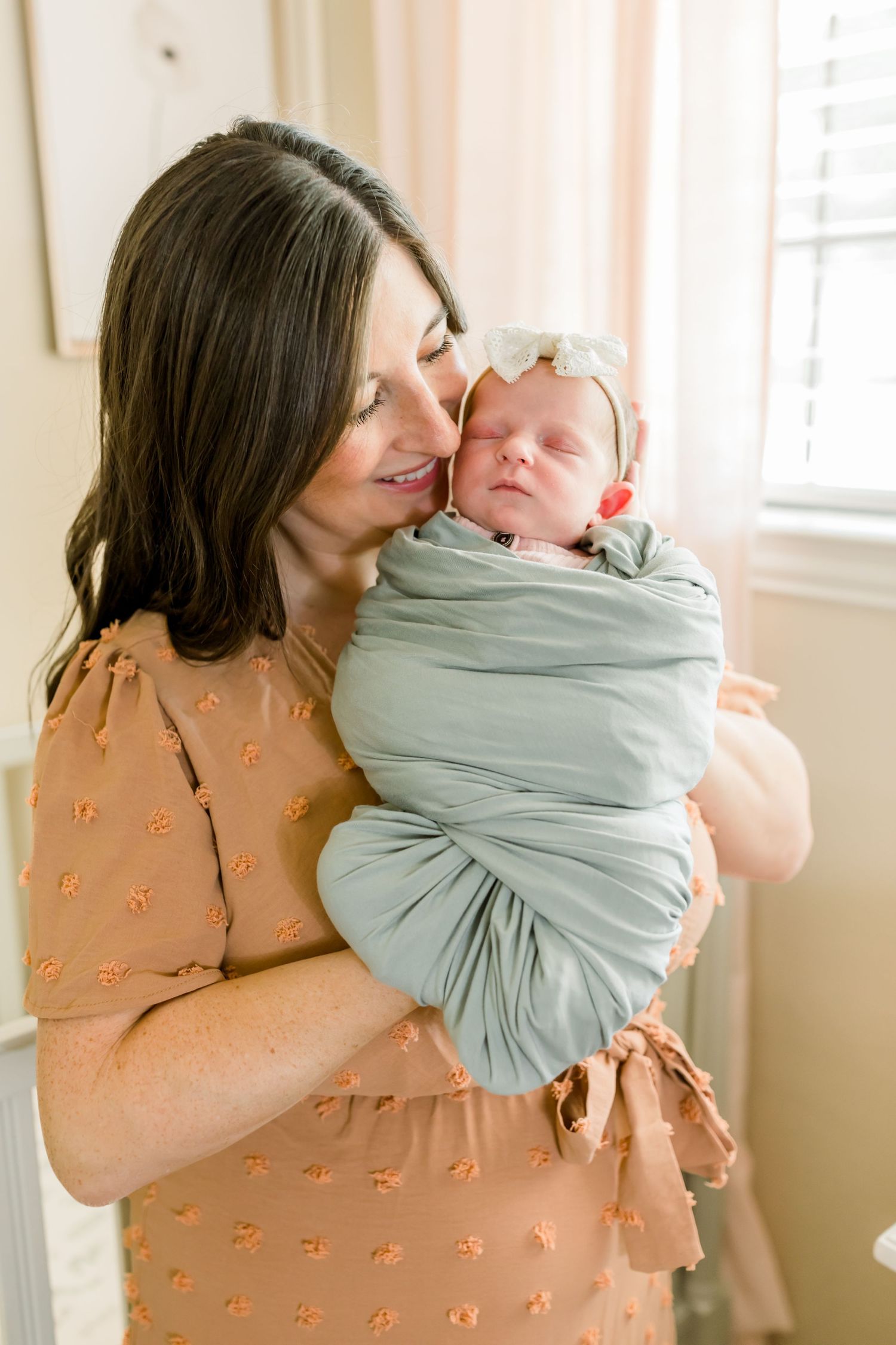 Intimate nursery portrait with caregiver embracing newborn in mint green swaddle wrap.