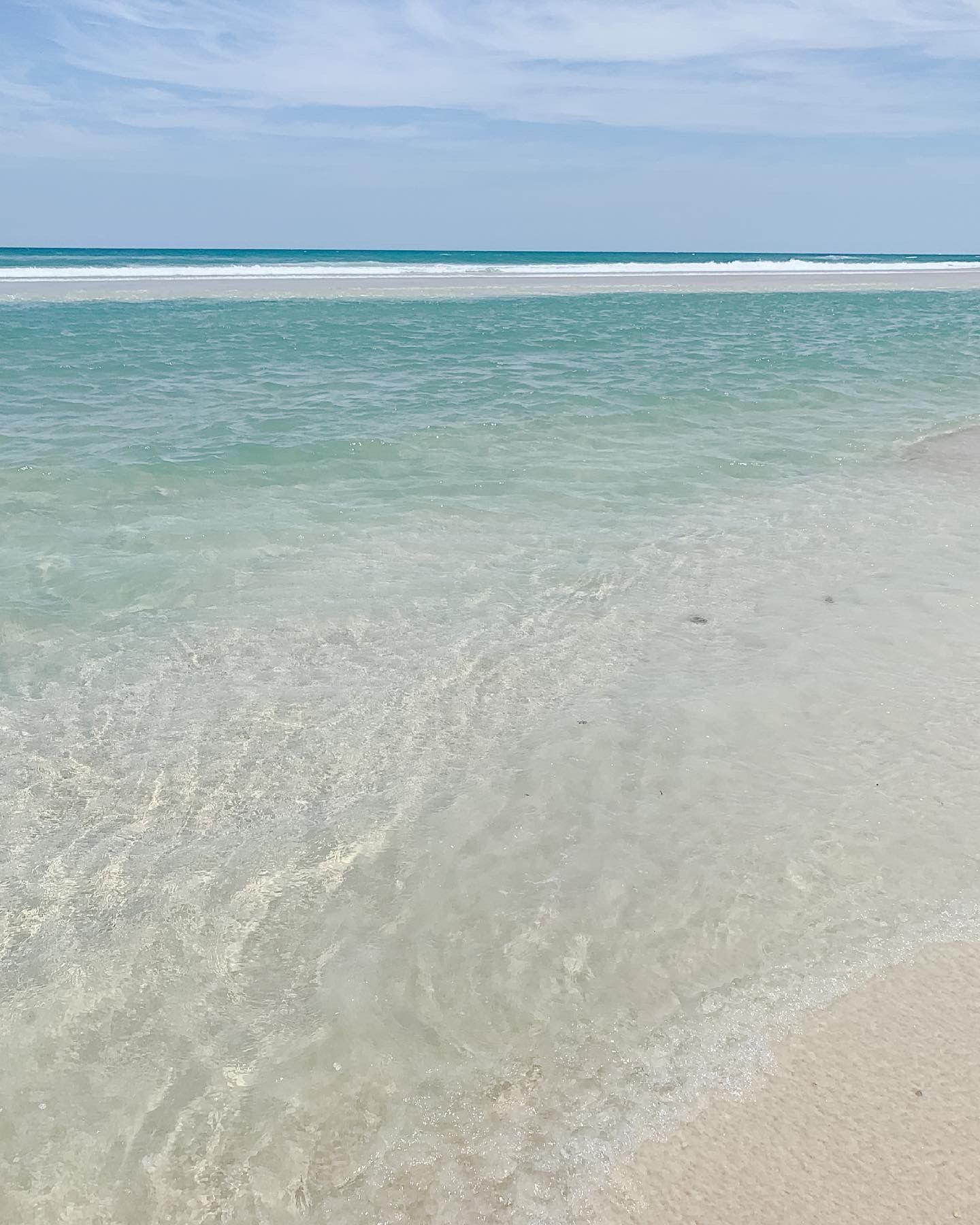 Crystal clear turquoise waters meet white sandy beach under bright blue skies.