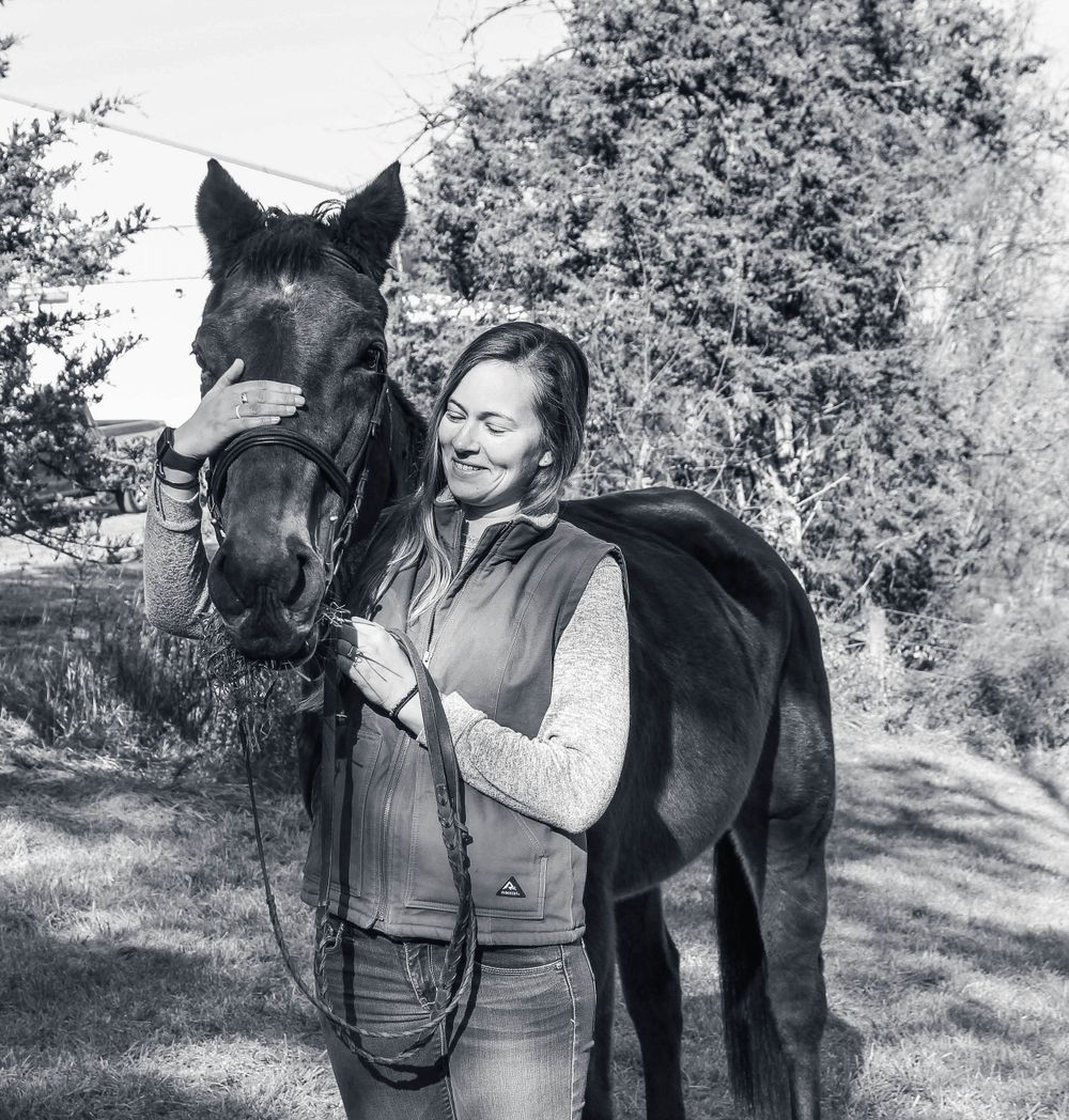 Black horse and rider standing together in a black and white outdoor photograph showing a close connection.