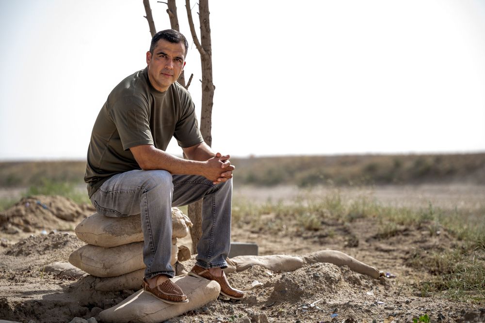 Man in olive shirt and jeans sitting on stacked rocks in arid landscape.