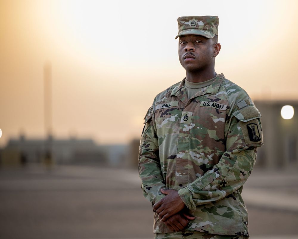 US Army soldier standing at ease in OCP camouflage uniform during golden hour at military base.