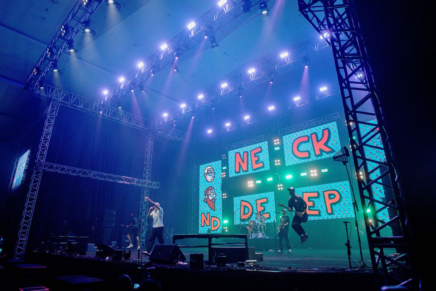 Concert stage with blue lighting and 'NECK DEEP' text display on large screens.