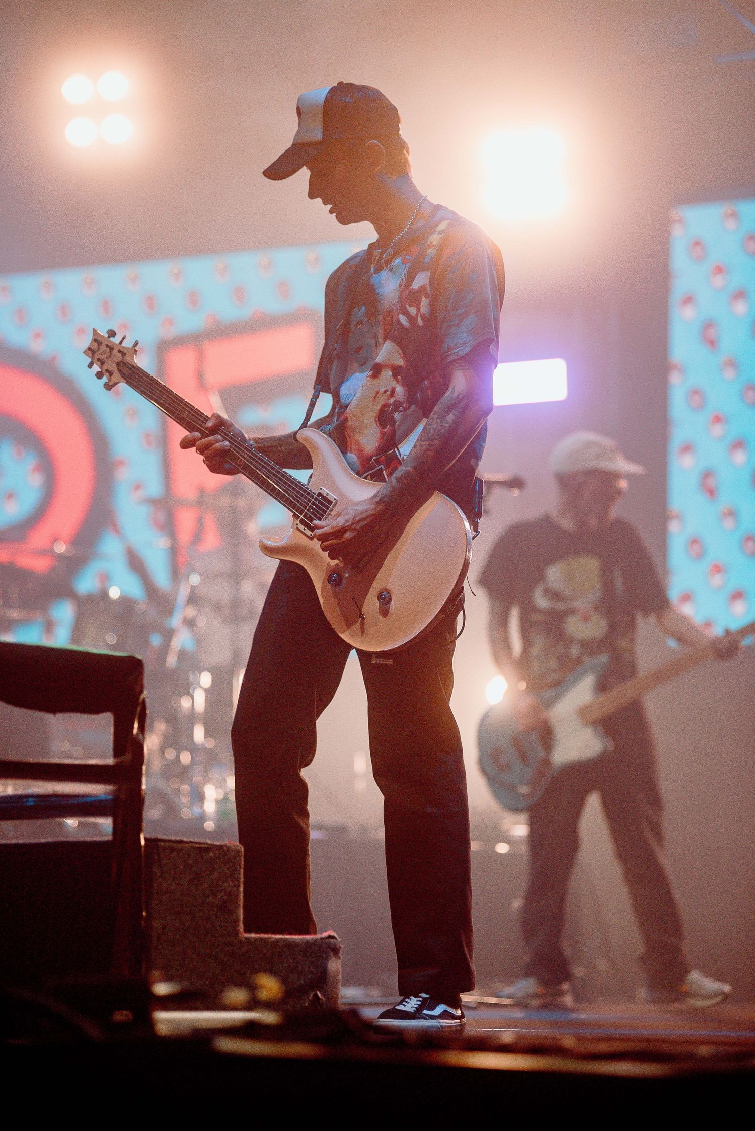 Guitarist performs on stage with backlit pink lighting and digital backdrop.