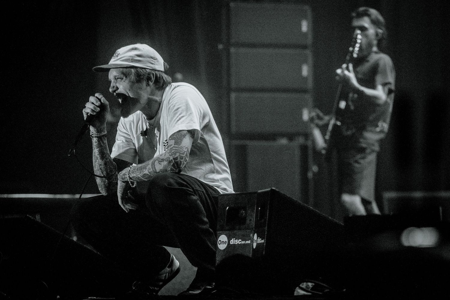 Black and white performance shot on stage with dramatic concert lighting.
