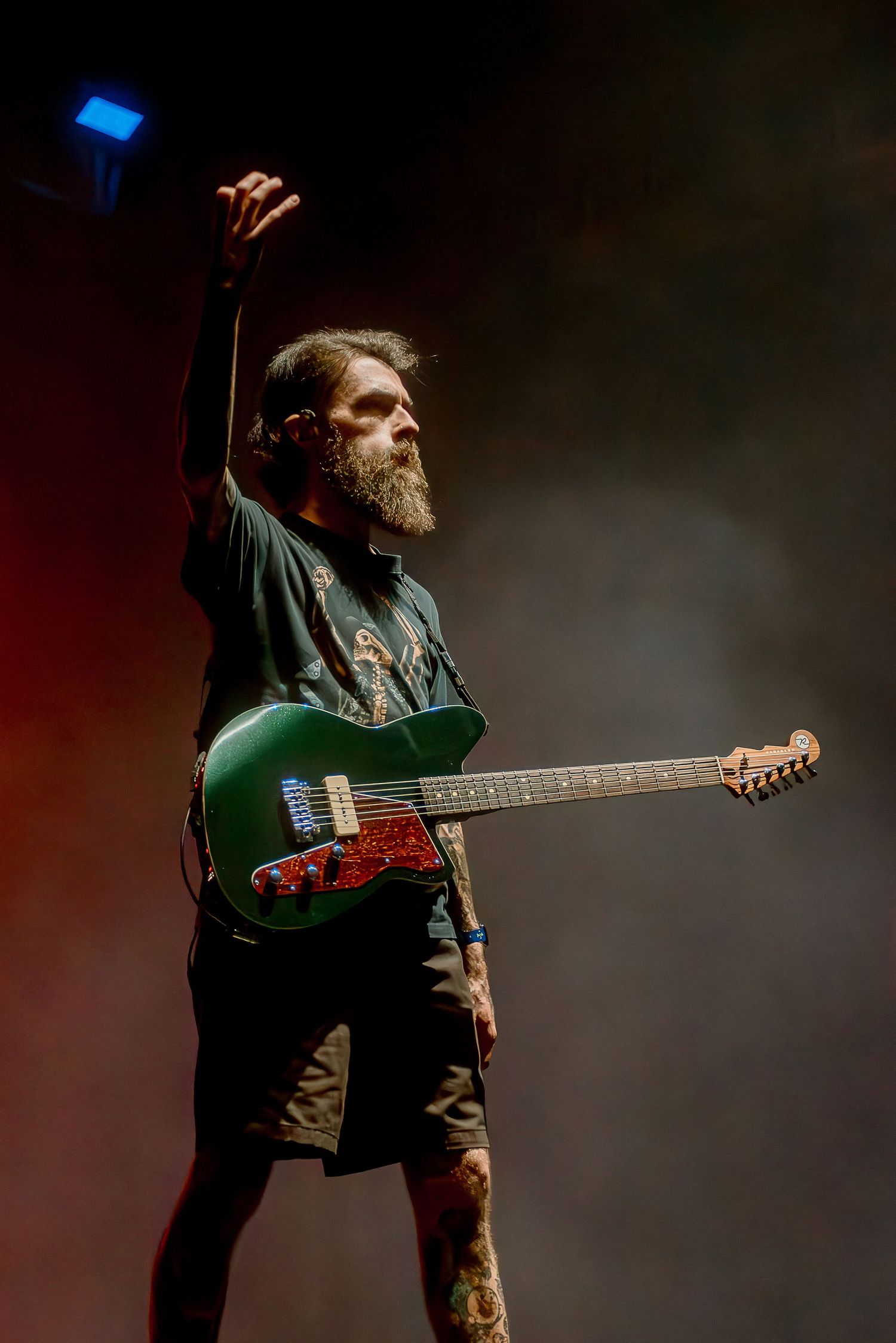 A performer in dark clothing plays a green electric guitar on stage with dramatic lighting.
