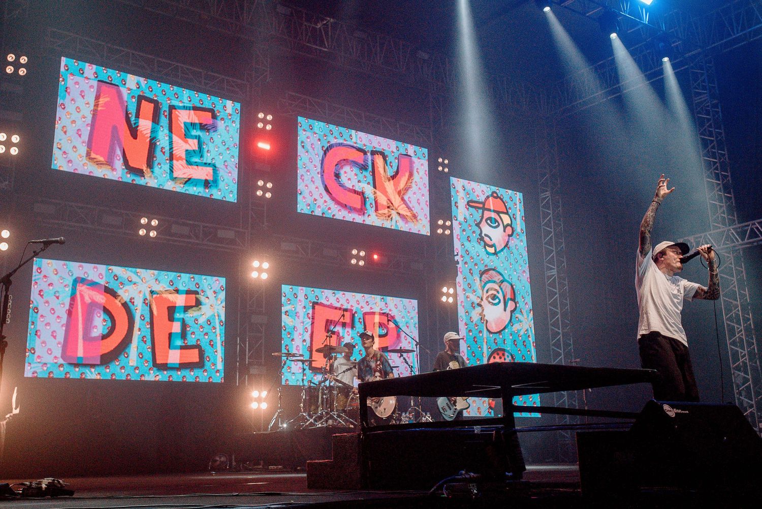 Stage performance with red illuminated 'NECK DEEP' text panels and dynamic lighting.
