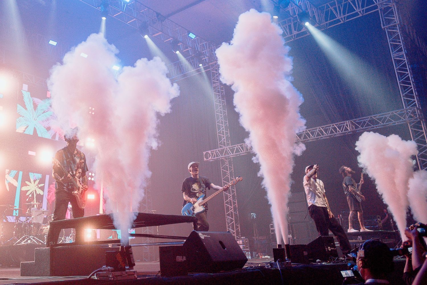 Rock concert stage with pink smoke effects and performers silhouetted against bright lights.