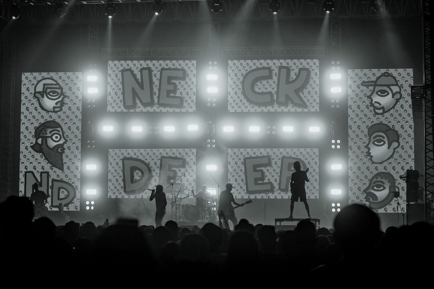 Black and white concert stage with illuminated 'NECK DEEP' text display and dramatic lighting.