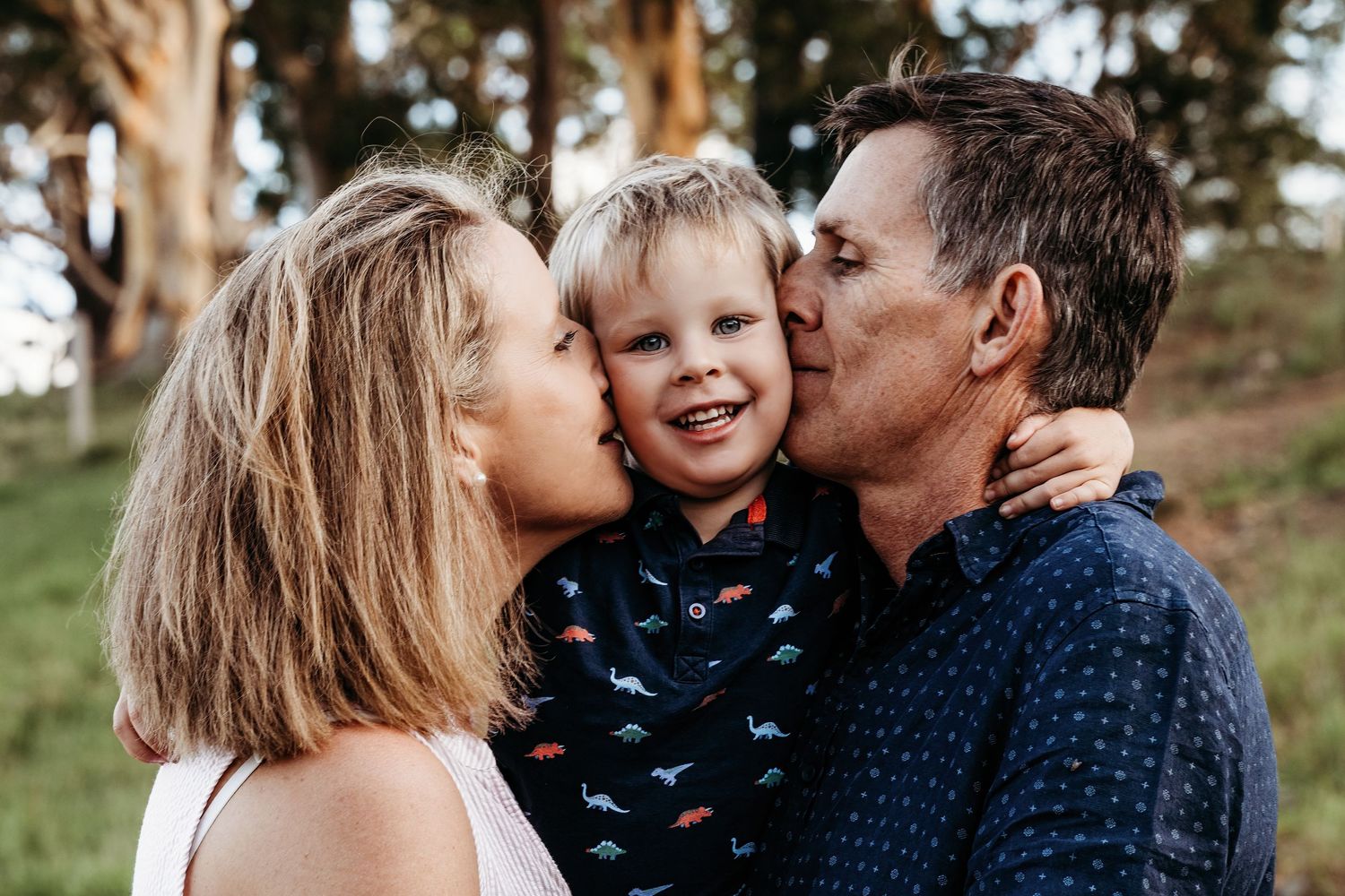 A tender family moment shared outdoors with trees in the background.